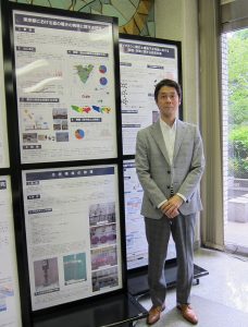 東京都環境科学研究所の1階ロビーには様々な研究成果のパネルが展示されている。「東京都における夏の暑さの実態に関する研究」のパネルの前にて(常松氏)
