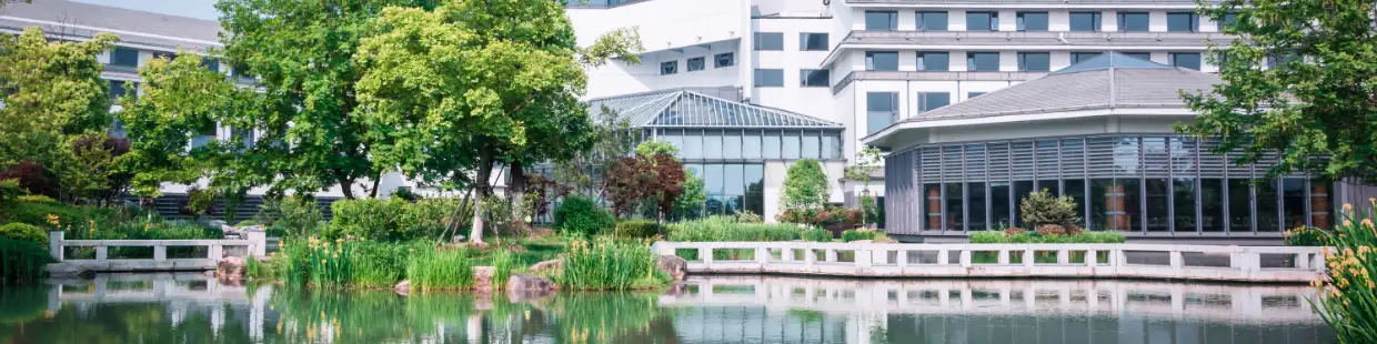 池と緑に囲まれた近代的な庁舎の建物が背景に写る。中央には温室のようなガラス張りの施設があり、白い橋や植栽が調和した整備された庭園が広がっている。中央省庁のイメージを象徴する景観。